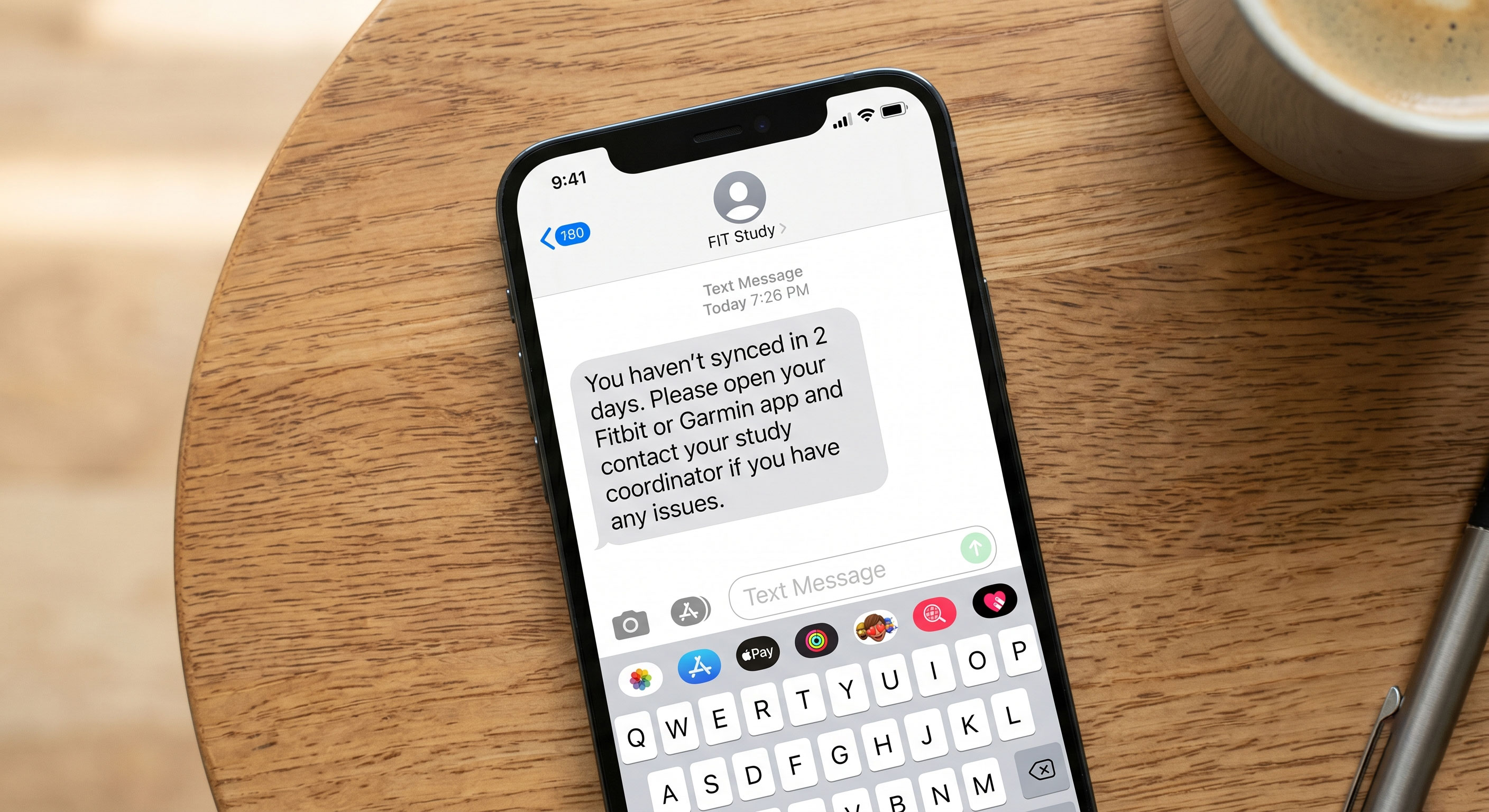 Smartphone on a wooden table showing an SMS reminder to sync from a study coordinator